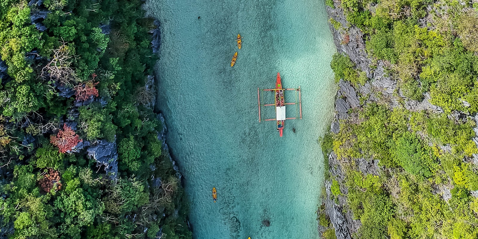 Aerial view of an outrigger boat and kayaks on turquoise water in Palawan, the Philippines