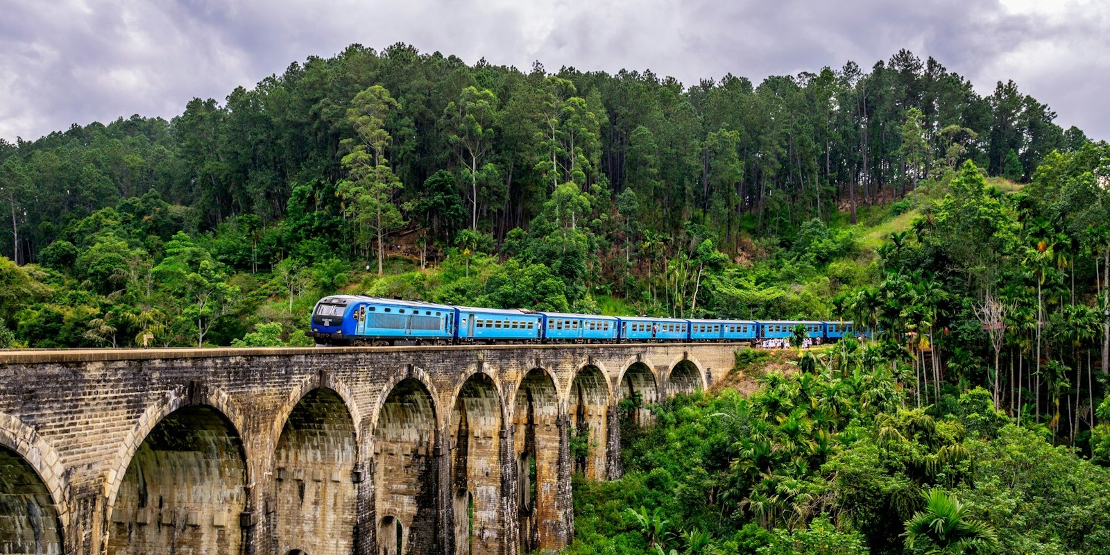A blue train winding through green hills in Sri Lanka